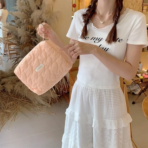 Close-up of quilted heart pattern on peach-colored cosmetic bag held by a model
