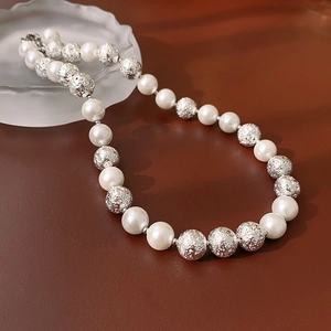 Detailed macro of a minimalist necklace with white pearls and textured silver metal beads