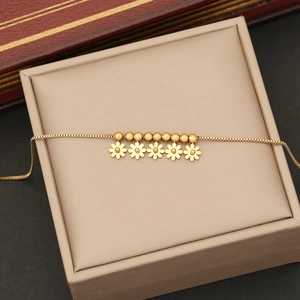 Close-up of golden stainless steel flower pendant with beaded chain on beige jewelry box