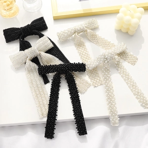 Detail of handcrafted beaded bow hair clips with pearls and rhinestones on white surface