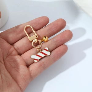 Close-up of a gold dog bone keychain with white enamel, red stripes, and small bell