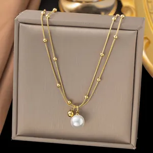 Detail of gold titanium necklace featuring a white pearl pendant on a grey display stand