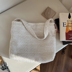 Détail macro du sac cabas en tweed crème montrant l'étiquette latérale et le tissu