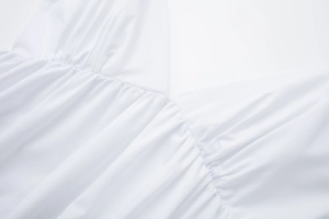 Close-up of white cotton midi dress showing refined fabric pleats and stitching detail