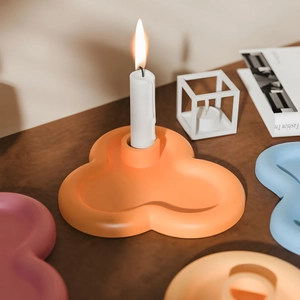 Detail of clover-shaped silicone candle holder in various pastel colors on a wooden table