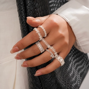 Close-up of stacked silver hollow lace flower rings on hand with a chic black background