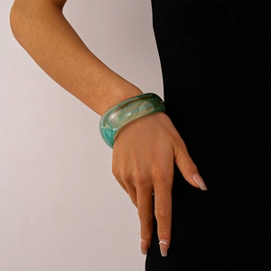 Close-up of wide acrylic bangle featuring green and brown marbled resin texture