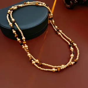 Retro faux tiger eye and gold pearl layered necklace draped on a dark jewelry box