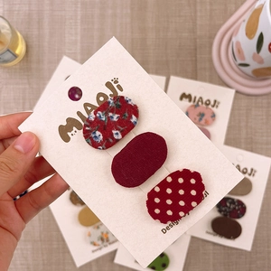 Dettaglio di tre mini fermagli ovali in tessuto con motivi floreali e a pois