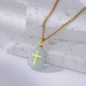 Macro view of gold dainty necklace with green stone pendant and cross inlay