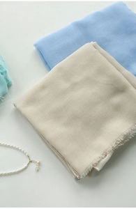 Detail shot of beige and blue linen scarves with fringe edges and pearl necklace accent
