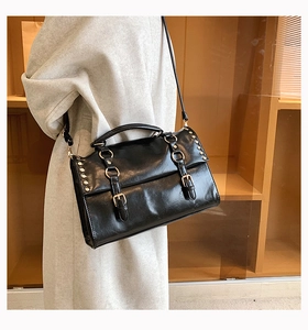 Detail of black vintage messenger bag with metal rivets and smooth glossy PU leather texture
