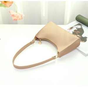 Detail of minimalist beige PU leather baguette bag with gold zipper and metal pendant
