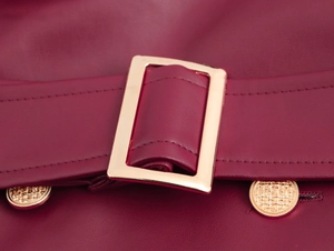 Detail van bordeauxrode PU-lederen jurk met gouden gespriem en getextureerde metalen knopen