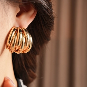 Close-up of golden multi-layer textured hoop earrings worn on ear with high-gloss finish