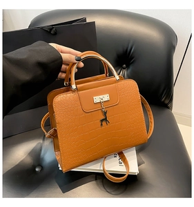 Détail du sac à main marron motif croco avec poignée dorée et pendentif cerf sur un siège
