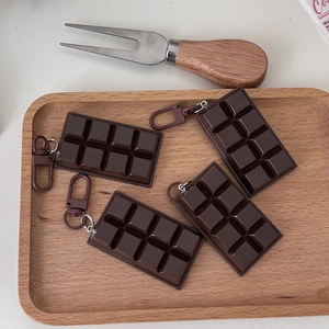 Close-up of four chocolate-shaped resin keychains with brown hooks on a wooden tray