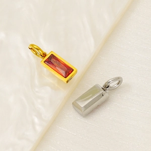 Detailed view of rectangular stainless steel pendants with red gemstone on ceramic plate
