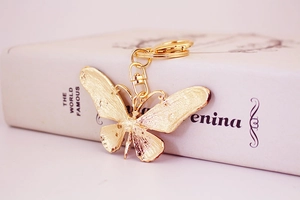 Detailed side view of a gold-toned butterfly keychain with textured wings on a book