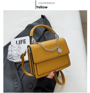 Detail of yellow crossbody bag with silver chain on a grey blazer in a stylish setting
