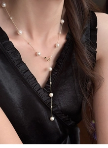 Detail of elegant Y-shaped gold pearl necklace draped on luxury black satin fabric