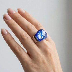 Gros plan détaillé d'une bague à gros cristal bleu et monture argentée portée au doigt