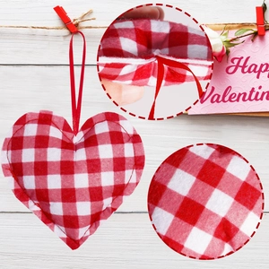 Detail of red gingham heart ornament with stitching and ribbon on white wood background
