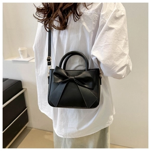 Detail of a black PU handbag with a large bow decoration shown on a model's shoulder