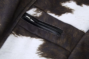 Macro detail of cow print faux fur jacket showing zipper with black leather trim
