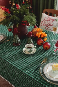 Green plaid Christmas tablecloth featuring snowflake patterns and white pom-pom fringe
