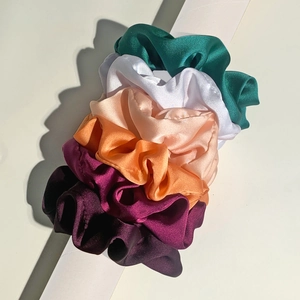 Detailed view of 5-piece satin scrunchies set in multi-colors stacked on a white cylinder