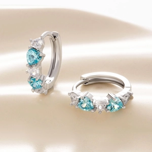 Silver hoop earrings with blue heart-shaped zircons on beige silk background