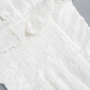 Close-up of white off-shoulder dress featuring floral eyelet embroidery and smocked details