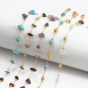 Detail of bohemian gold chains with colorful natural crushed stone beads on a white stand