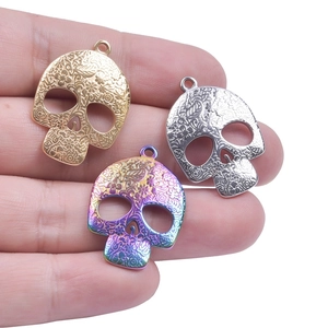Skull pendant set in gold, silver, and rainbow steel with intricate cutout floral patterns