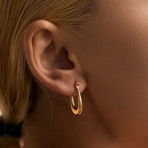 Detailed close-up of polished gold U-shaped hoop earrings worn on a model's ear
