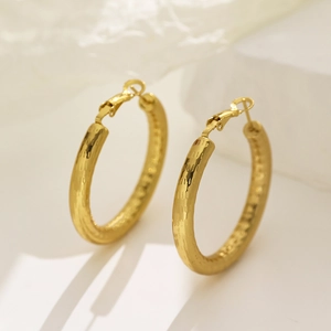 Minimalist gold hoop earrings with hammered texture finish on white stone backdrop