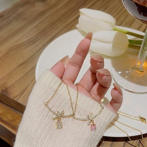 Elegant gold bow necklaces with pink and white teardrop gems on a wooden surface