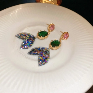 Detailed close-up of pink and green mermaid tail earrings on a white ceramic plate