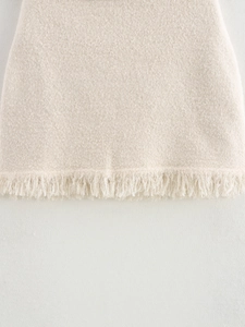 Detailed close-up of beige knitted skirt featuring fringe tassel hem and wool-like texture