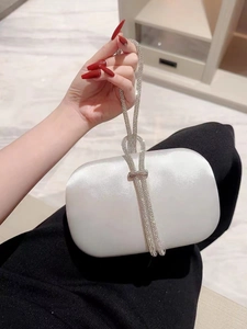 Close-up of pearl white satin evening clutch with sparkling rhinestone woven handle