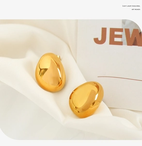 Detailed view of chunky golden teardrop earrings on elegant white satin fabric