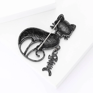 Detailed view of a black alloy cat brooch with a dangling fishbone pendant on a white stand