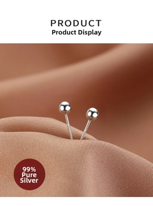 Macro detail of minimalist 999 sterling silver ball stud earrings on brown satin fabric