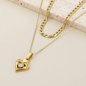 Detail view of gold-layered necklace featuring a crystal heart pendant on travertine stone