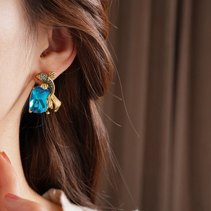 Close-up of vintage golden fish earrings with blue rhinestones worn by a female model