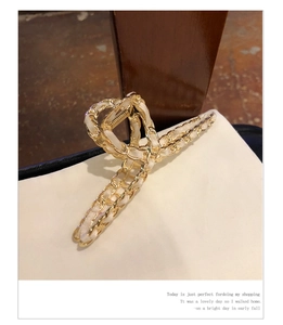 Detail view of a golden metal jaw clip woven with elegant white ribbon and chain link
