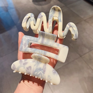 Close-up of three large cream-colored hair claws with elegant lavender floral patterns
