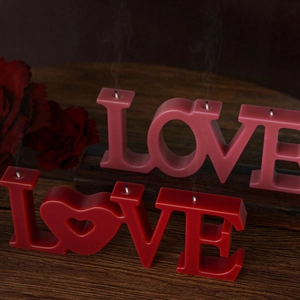 Detailed close-up of red and pink LOVE letter candles with heart-shaped O on dark wood