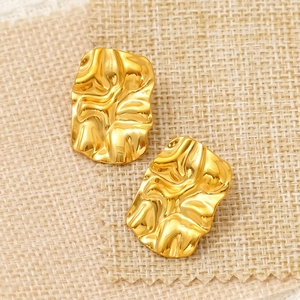 Golden irregular geometric crinkle texture stud earrings on a beige linen surface